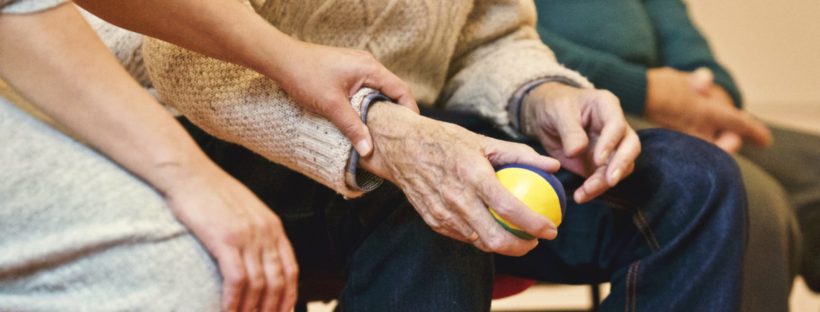 An older woman holds on to an older man's arm with a ball in it while they are sitting down