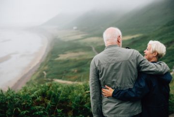 A sweet elderly couple on a green mountain with a view of a misty ocean